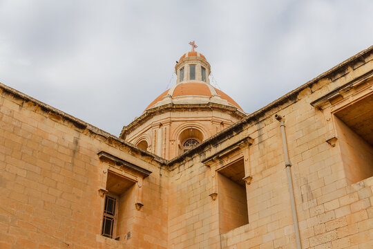 View of the striking dome of the Parish Church casting a warm glow against the cloudy sky, a beacon of faith and architecture, Marsaxlokk, Malta.