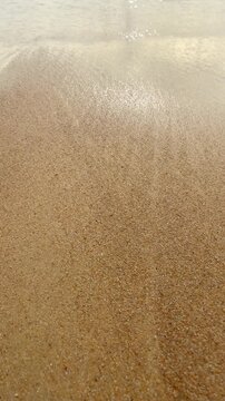 Ocean wave retreating from sandy shore close-up, vertical video of sea foam on tropical beach, nature background.