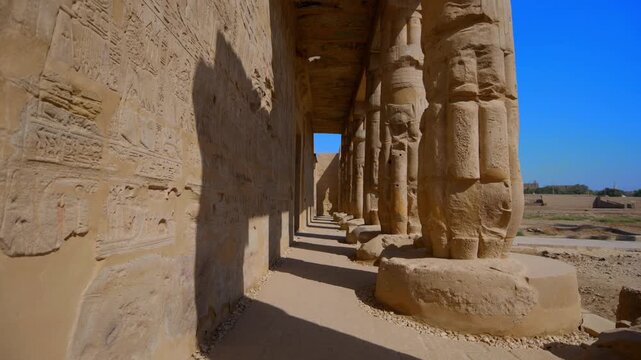 Osiride colonnade with hieroglyphic wall at Seti I mortuary temple, Luxor Egypt. Dramatic perspective of ancient pillars and statues against vivid blue sky. Travel and history.