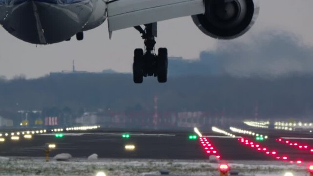 A large passenger airplane lands on an airport runway in winter. Close up view from behind as the landing gear touches down, creating smoke on the wet, snowy tarmac. Filmed in slow motion