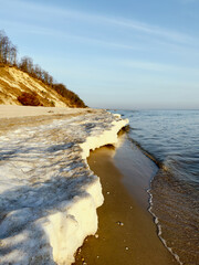 dramatic coastal scene featuring a thick ledge of ice and frozen sand along a beach, with steep sandy cliffs in the background