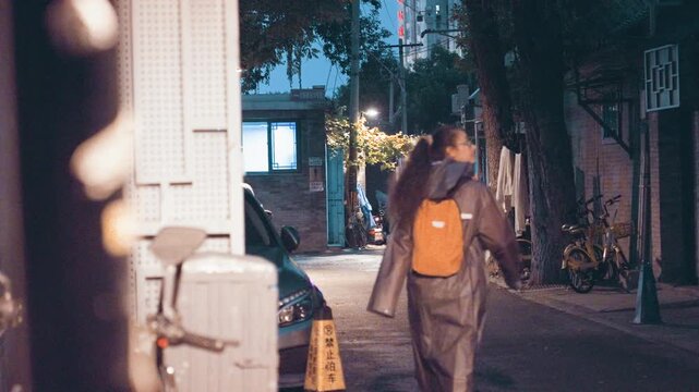 Student walks alleyway quietly. Evening commute along shadowed narrow passage. Student leisurely moves through secluded alley illuminated by distant string lights and reflective surfaces