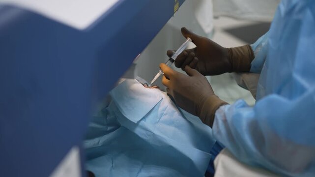 Close up video of a surgeon in scrubs performing a delicate eye operation on a patient in a modern clinic. The doctor uses a syringe and other instruments near the patient's eye. Medical procedure