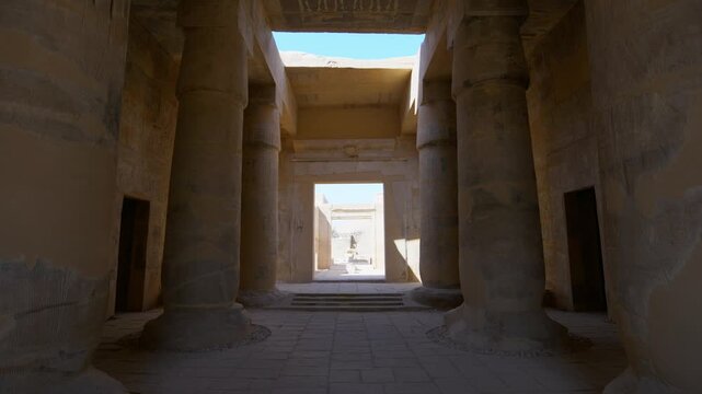 Osiride colonnade with hieroglyphic wall at Seti I mortuary temple, Luxor Egypt. Dramatic perspective of ancient pillars and statues against vivid blue sky. Travel and history.