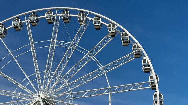 Low-angle view of a large, white modern Ferris wheel with glass gondolas against a deep blue, cloudless sky