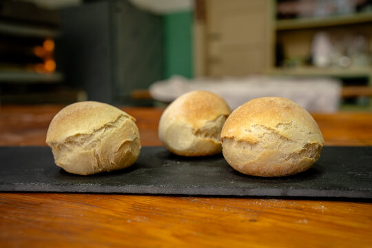 Freshly baked bread rolls on a black tray in a bakery during the afternoon