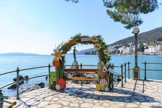 Easter themed decorative arch with bench overlooking the Adriatic Sea and view of the Opatija coastline and the &ldquo;Maiden with the Seagull&rdquo; statue. Traditional seasonal installation