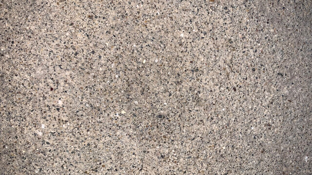 A rough, speckled concrete surface texture in close-up, showcasing embedded small aggregate stones in mixed grey and brown tones, perfect for versatile material backgrounds.