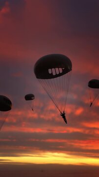 Group of people flying with parachutes in the sky as silhouettes appear against glowing sunrise horizon