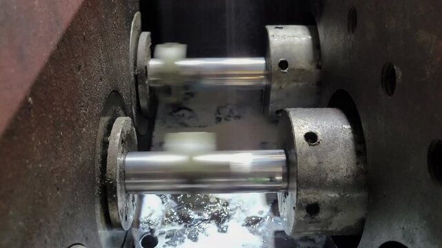 Macro shot of high-pressure emulsion pump piston rods moving back and forth. Detailed view of packing glands, metallic wear, and lubricant texture in a heavy-duty industrial factory environment.