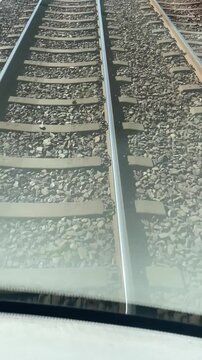 Ballast railway tracks viewed through window, close perspective over gravel and sleepers, coarse stone texture and railhead glint, muted