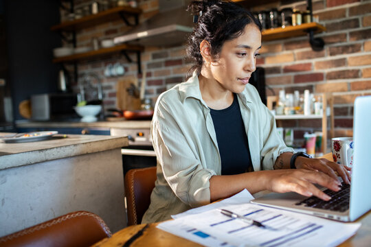 Young woman working on laptop at home kitchen table