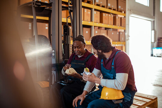 Two warehouse workers eating lunch by forklift