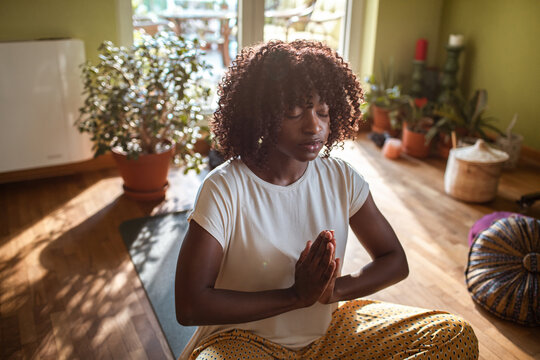 Young woman meditating with prayer hands in sunny home living room
