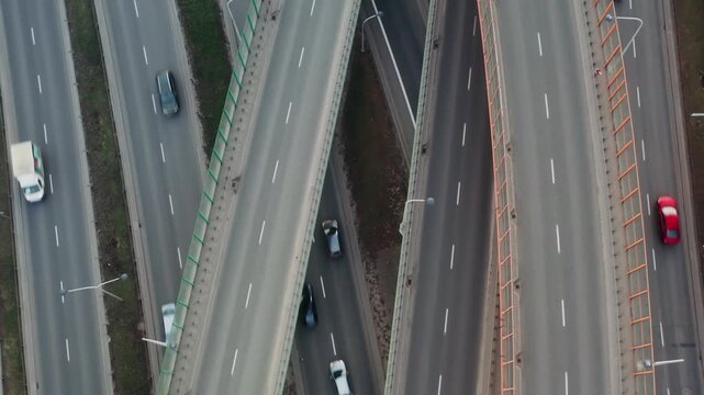 Aerial top view complex highway interchange with overpasses and multilane roads. Cars move through structured junction, forming geometric patterns. Urban transport network in daylight