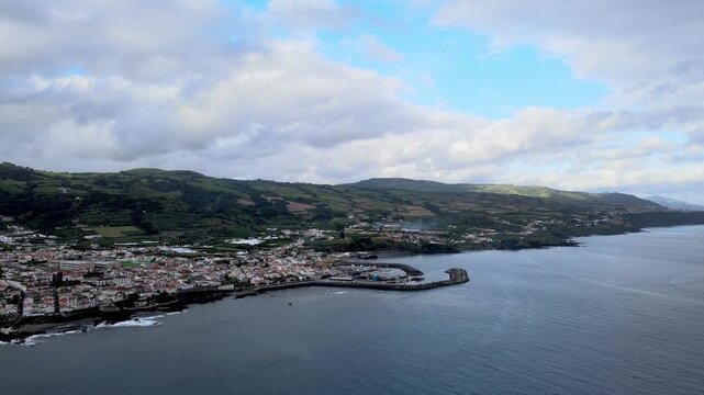 Aerial drone view of Vila Franca do Campo on S&atilde;o Miguel Island. From high altitude, the coastal town is visible with red-roof houses, agricultural fields and green landscape. The harbor and marina ext