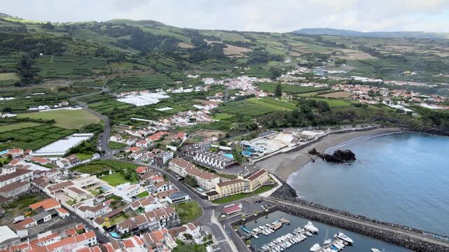 Aerial drone view of Vila Franca do Campo on S&atilde;o Miguel Island. From high altitude, the coastal town is visible with red-roof houses, agricultural fields and green landscape. The harbor and marina ext