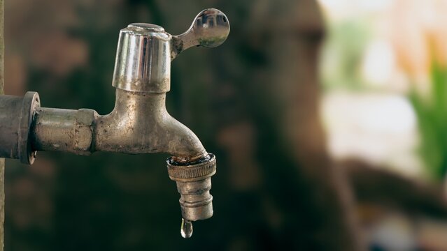 Old metal water tap dripping outdoors with bokeh background
