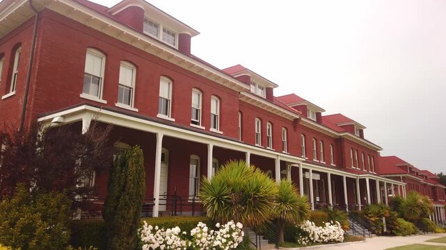 Pan across historic red brick barracks with covered porches and dormer windows on an overcast day