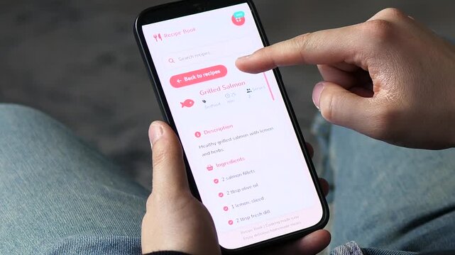 Close-up of someone choosing a recipe on a mobile app at home. User scrolls through healthy meal options and selects grilled salmon. Perfect for lifestyle, cooking, and healthy eating content.