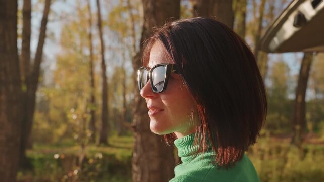 Caucasian woman with short hair revels in vibrant outdoor adventure during fall. Joyful woman embarks on picturesque outdoor autumn excursion beneath sunny sky with cheerful expression