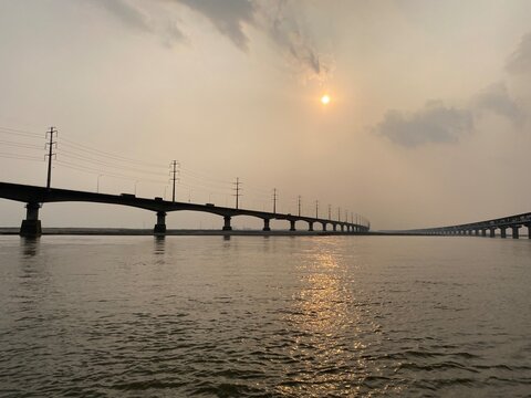 Beautiful sunset over Jamuna river and the Jamuna Bridge. Colorful reflections in the water. Sunset on the river bridge. Railway bridge at beautiful sunset. Sunset through a bridge.