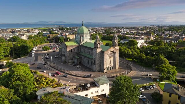 Aerial view of Galway Cathedral in Ireland. Majestic panorama of Galway city with grand cathedral, lush green trees, traditional Irish buildings that surround the site, and Atlantic Ocean on horizon