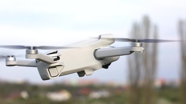 White drone flying in air with rotating propellers during cinematic aerial flight over park