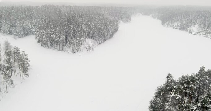 Aerial view of snow-covered landscape of frozen Kaitalampi lake winding through a dense, snow-draped boreal forest in cloudy winter weather, Espoo, Finland, Europe.