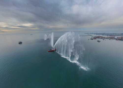 Panoramic aerial view of a fireboat performing a water salute in the port of Thessaloniki, Greece.