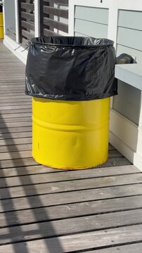Vertical view of a yellow trashcan with a black plastic bag liner that is blowing in the wind on the boardwalk
