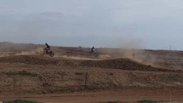 Aerial drone footage of motocross cross country race, dirt bikes speeding on rugged track, riders competing in off-road extreme motorsport event, dynamic action and dust clouds