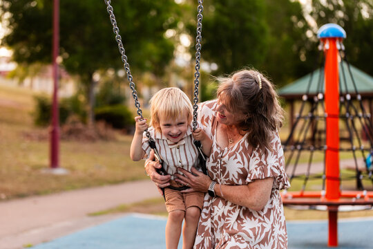 Happy grandmother playing with grandchild on swing at park on hot afternoon in Australia