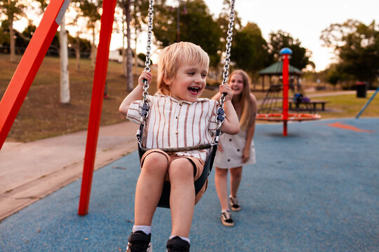 Happy autistic boy playing on swing at park with mother swinging him