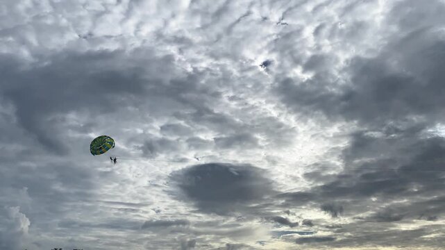 Tourists parasailing over dramatic cloudy sky along the beach in Phuket Thailand, adventure water sport activity.