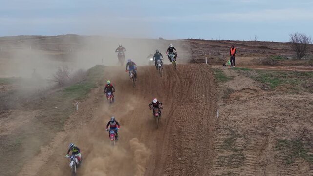 Aerial drone footage of motocross cross country race, dirt bikes speeding on rugged track, riders competing in off-road extreme motorsport event, dynamic action and dust clouds
