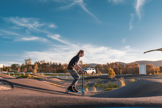 Teen boy riding scooter over jumps at pump track