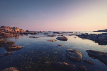 Obraz premium Serene rocky coastline at sunset with calm water and clear sky