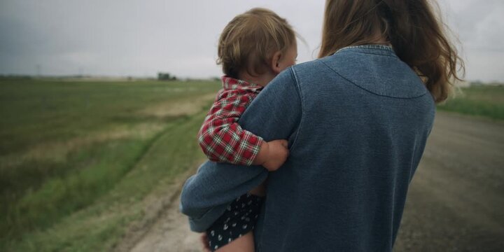 Mother giving a toddler a piggyback ride on a country road
