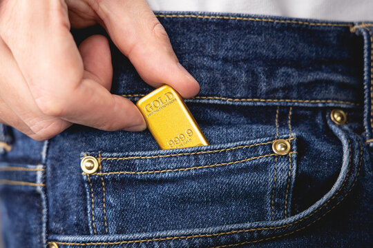 Gros plan d'une main tenant un lingot d'or dans la poche d'un jean.