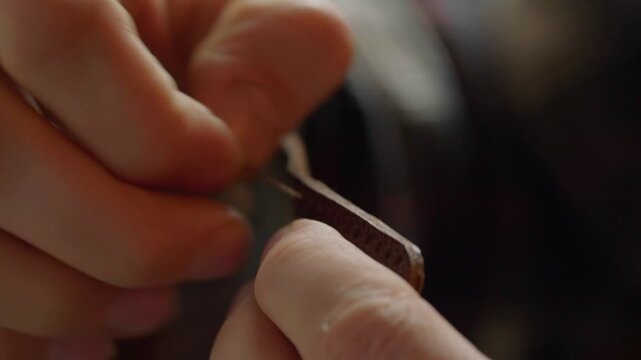 A very detailed close-up shot focusing on the two needles and thick, waxed thread as a craftsman performs a traditional saddle stitch on natural brown leather.