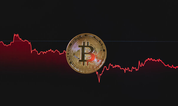 Une pi&egrave;ce repr&eacute;sentant le Bitcoin au centre. En arri&egrave;re-plan, on voit un graphique de march&eacute; rouge qui descend, indiquant des pertes et liquidations sur le prix de la cryptomonnaie.