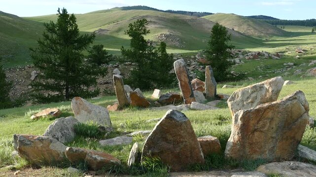 Stone slabs of ancient burial structures (Kheregsuurs) in the Mongolian steppe on the background rocky mountain. Summer sunny evening.  Landscape of Mongolia.