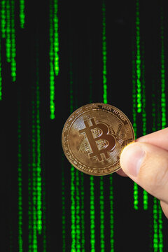 Une pi&egrave;ce Bitcoin tenue par une main, devant un fond de code vert, symbolisant la technologie blockchain, la cybers&eacute;curit&eacute; et l&rsquo;univers des cryptomonnaies. Le format est vertical.