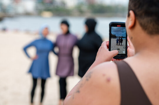Woman taking photos of women in burkinis using her phone on the beach