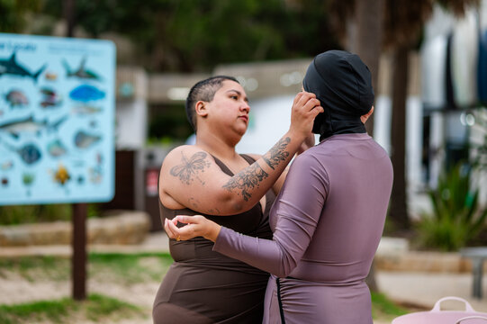 Woman in brown swimsuit fixing the headscarf of the other woman in burkini