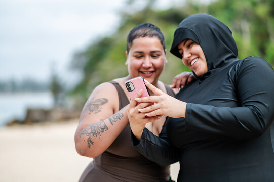 Multiracial women checking their phone on the sandy shore at the beach