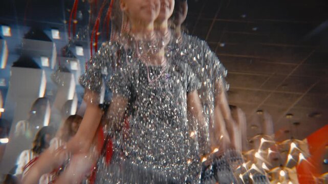 A young girl in a silver sequin dress dances happily at a party. The video uses a special prism lens to create a surreal, overlapping kaleidoscope effect, showing her energetic and joyful movements