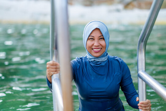 Filipina woman in a light blue headscarf holding on to metal handrail getting off the ocean pool