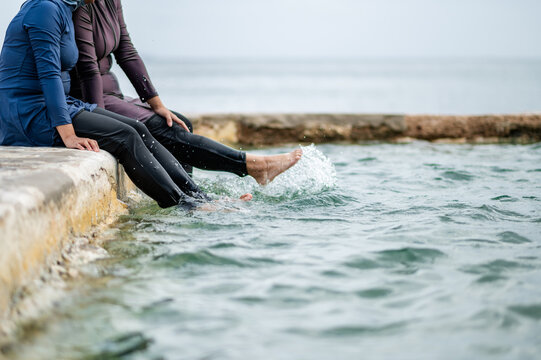 Womens legs paddling in tidal pool waters while sitting on stone platform